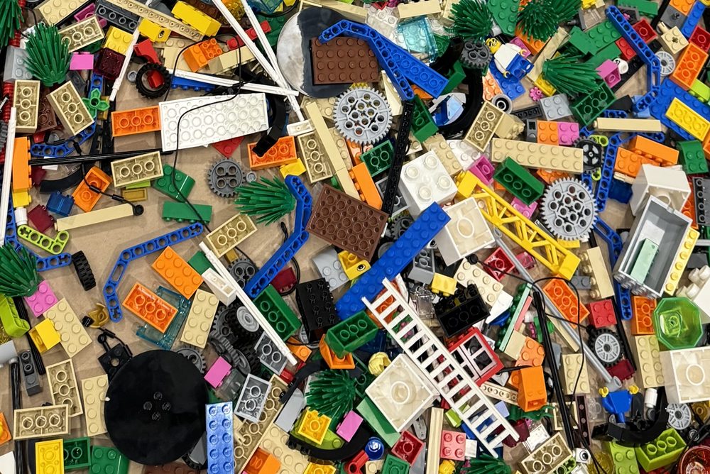 Vue de dessus d’un tas dense de briques LEGO® SERIOUS PLAY® multicolores : plaques, poutres bleues, engrenages gris, échelles blanches, frondes vertes, roues, pièces translucides et éléments de figurines