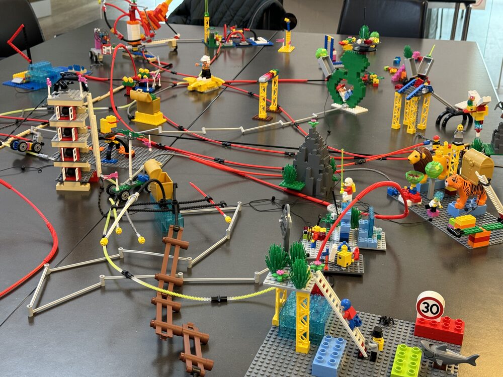Table d'atelier couverte de modèles LEGO® SERIOUS PLAY® posés sur des plaques, reliés entre eux par des tubes souples rouges et jaunes